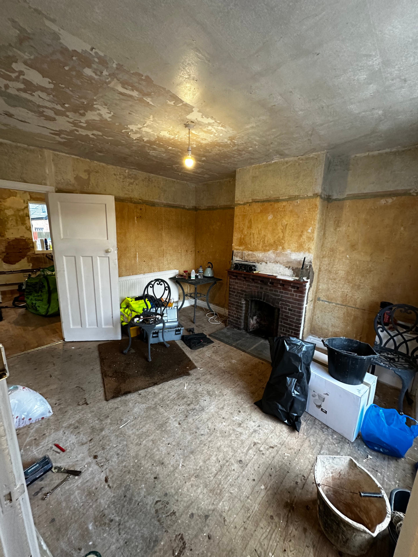 Stripped reception room with bay window, peeling plaster and original brick fireplace before works