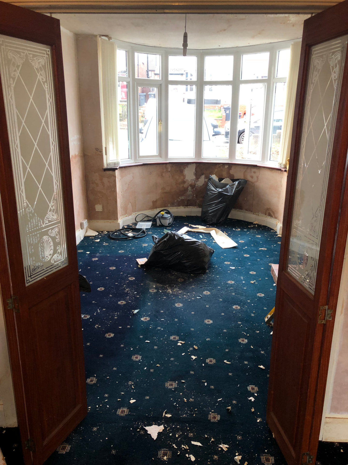 Living room before works with bay window, damp walls and old patterned carpet
