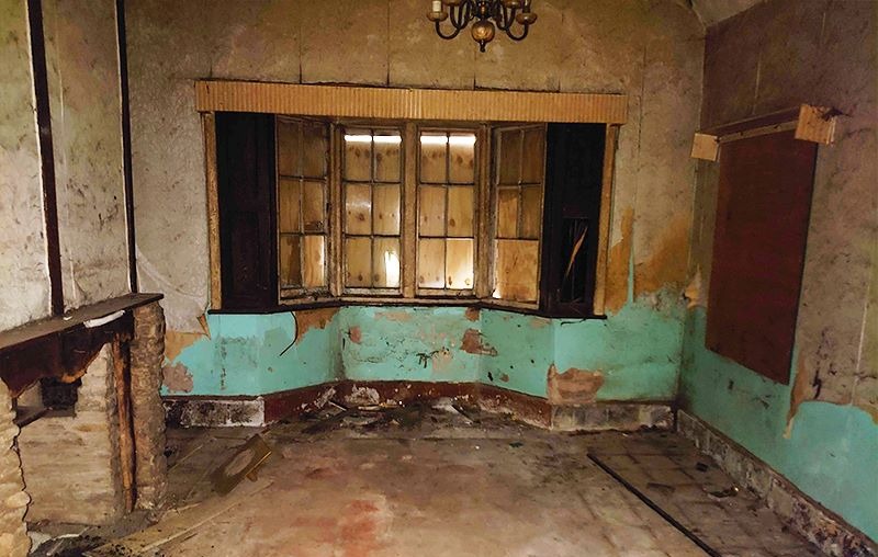 Stripped reception room with bay window, damaged plaster and original fireplace before works