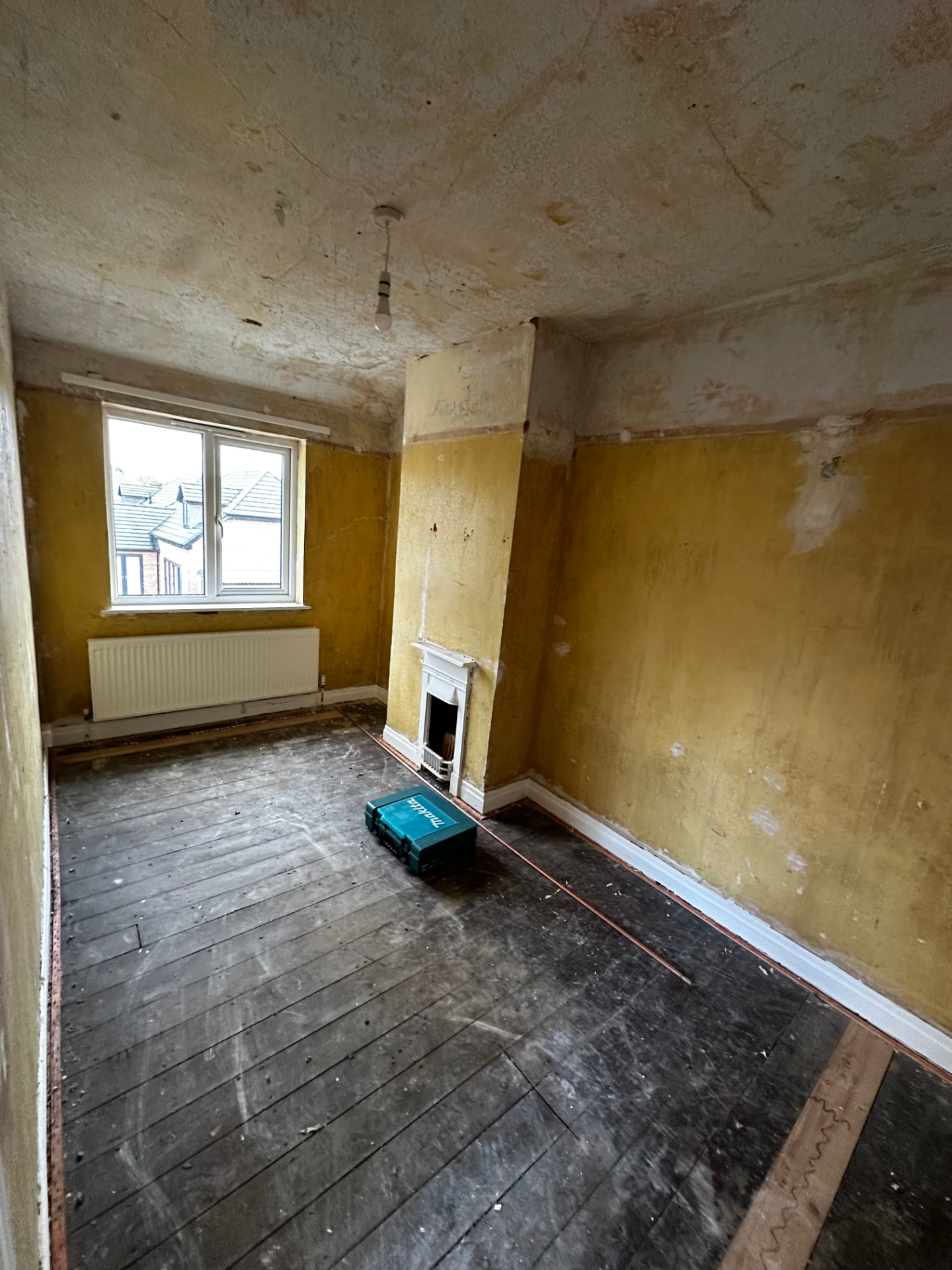Bedroom stripped to bare floorboards with damaged plaster and original fireplace before refurbishment