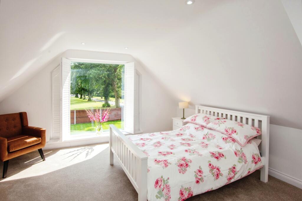 Loft bedroom with shuttered window overlooking the garden and leather armchair