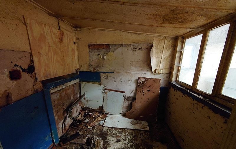 Stripped kitchen area with damaged walls and original floor tiles before refurbishment