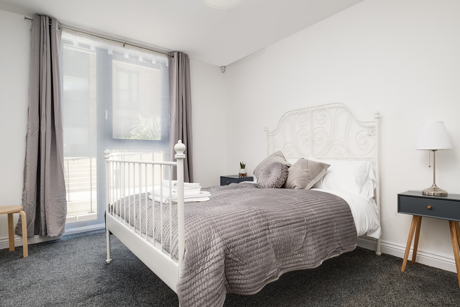 Calm bedroom with white iron bedstead, navy bedside tables and grey bedding