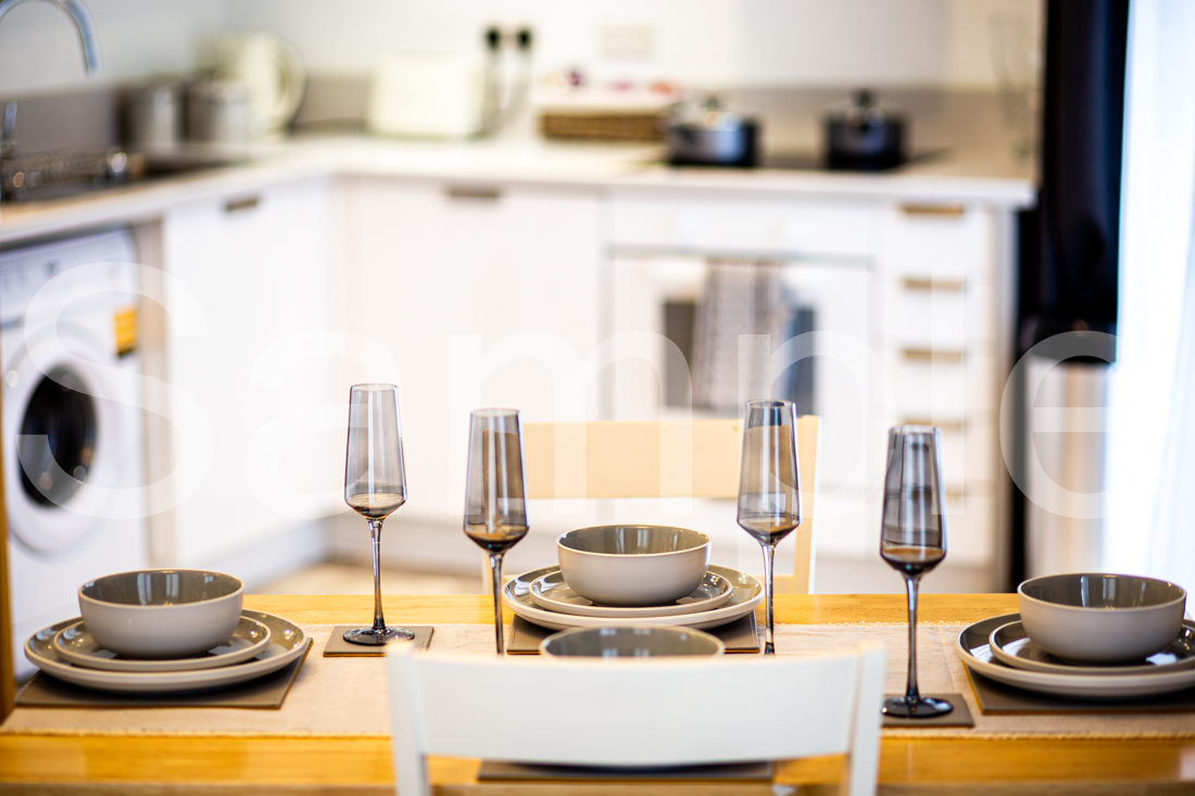 Dining table dressed with glassware and crockery in front of a fitted kitchen