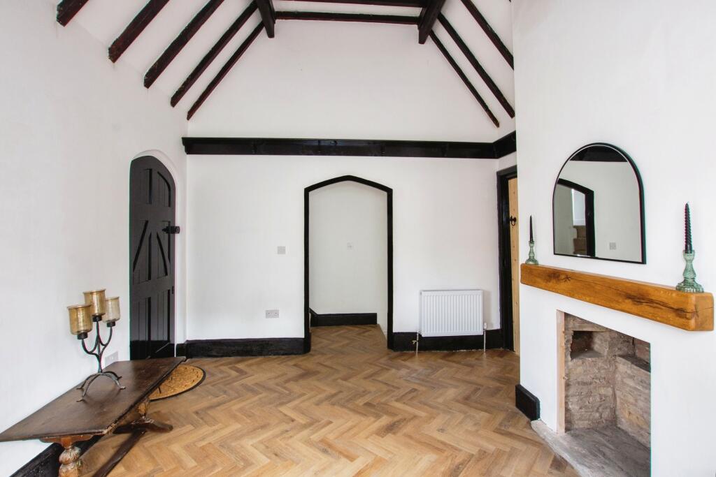 Entrance hall with exposed dark timber beams, arched door and stone fireplace