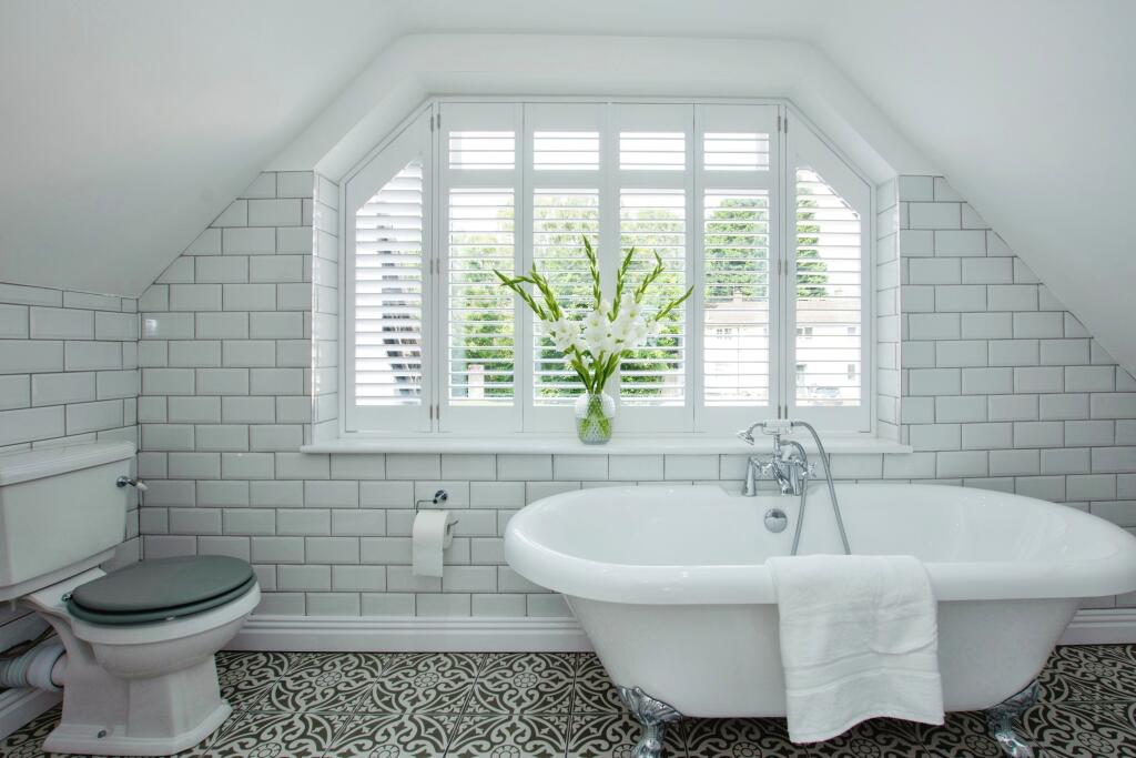 Bathroom with roll-top bath, metro tiling, patterned floor tiles and shutters