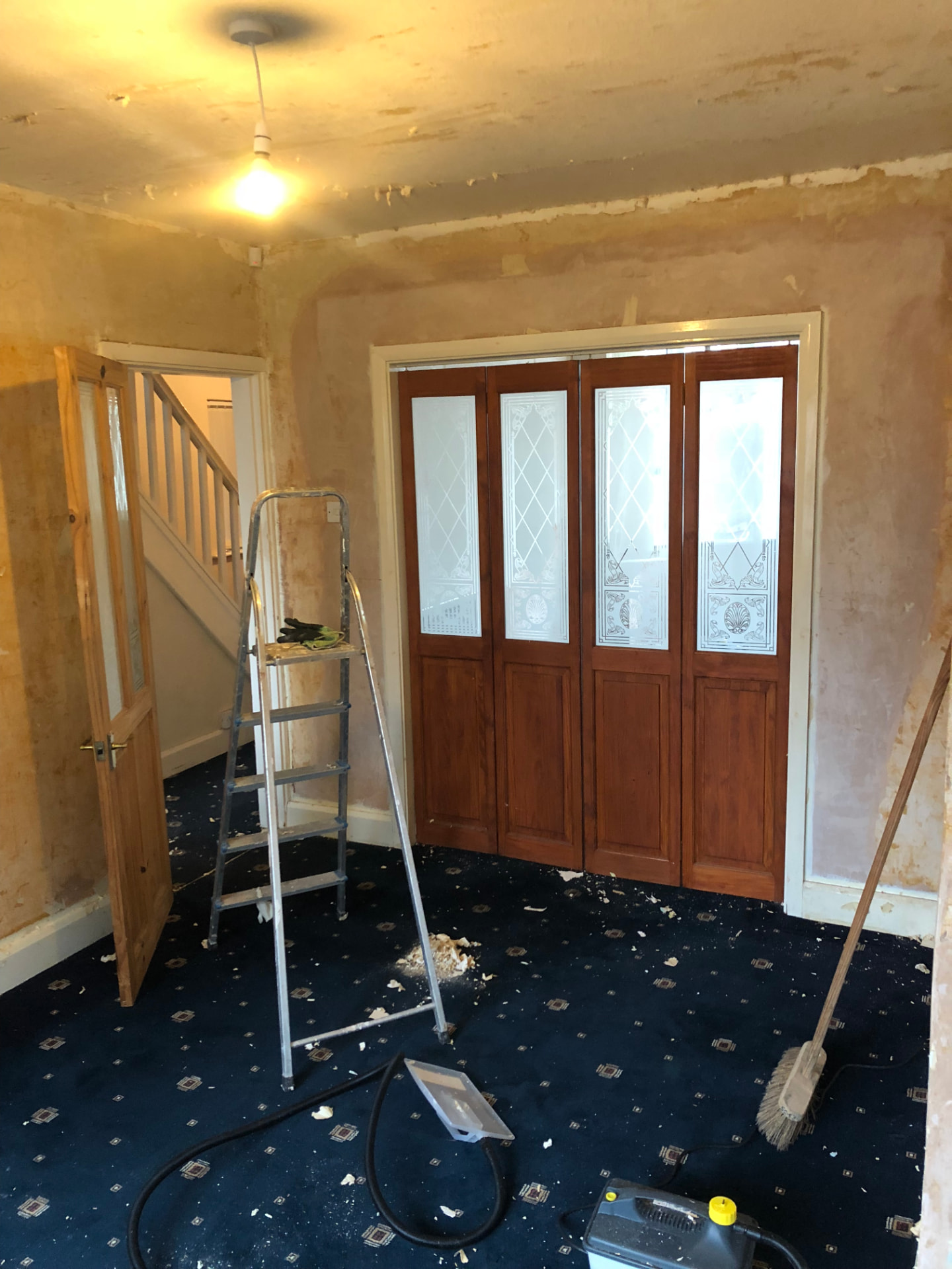 Entrance hall before works with stripped walls, dated timber doors and worn carpet