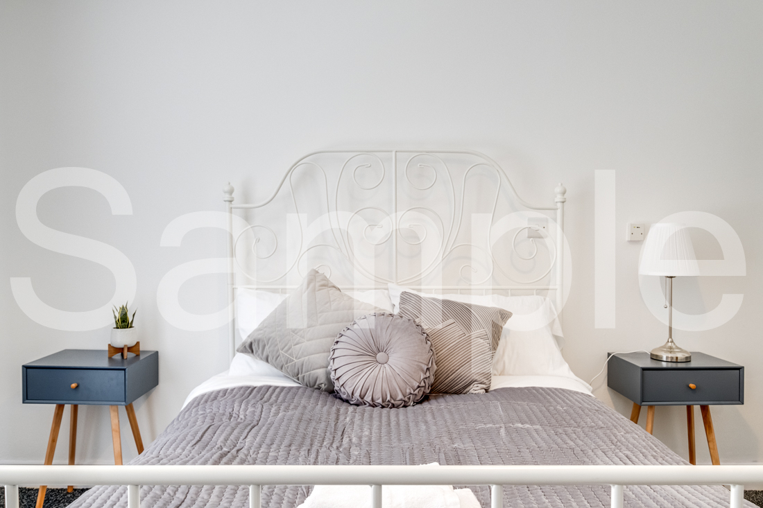 Calm bedroom with white iron bedstead, navy bedside tables and layered bedding