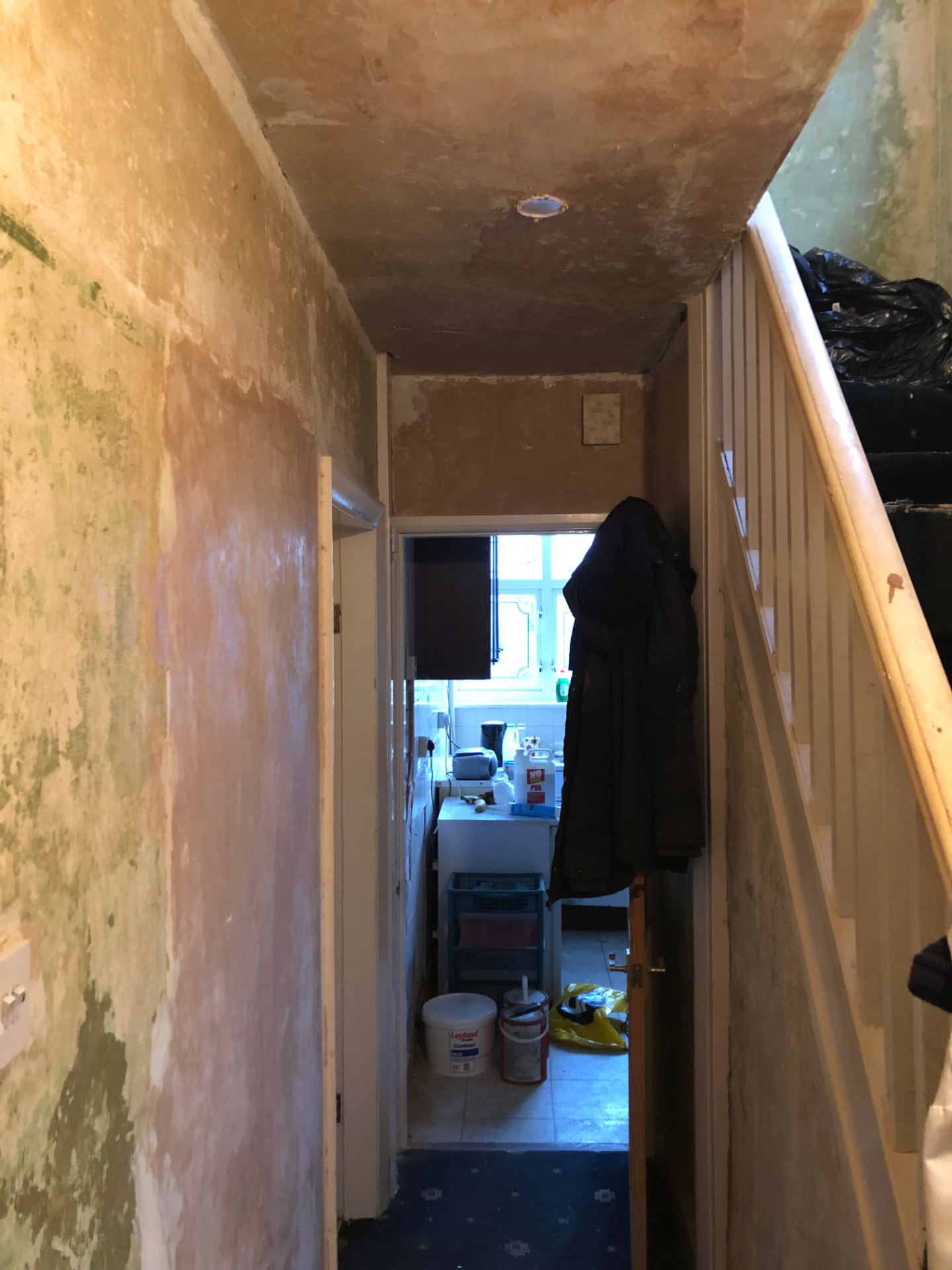 Hallway before works with damp stained walls and dated staircase